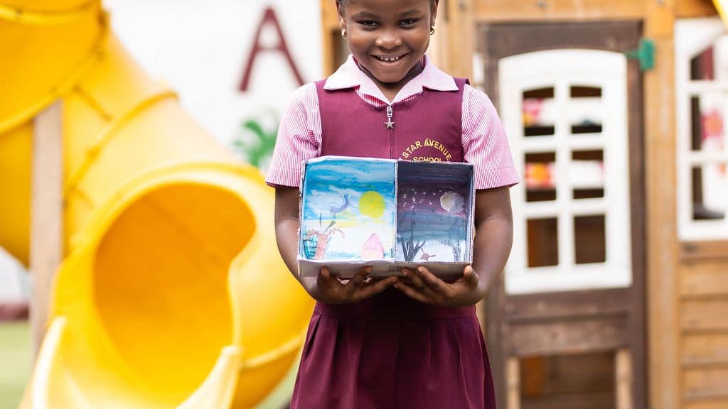 A pupil holding her project in front of the school playhouse