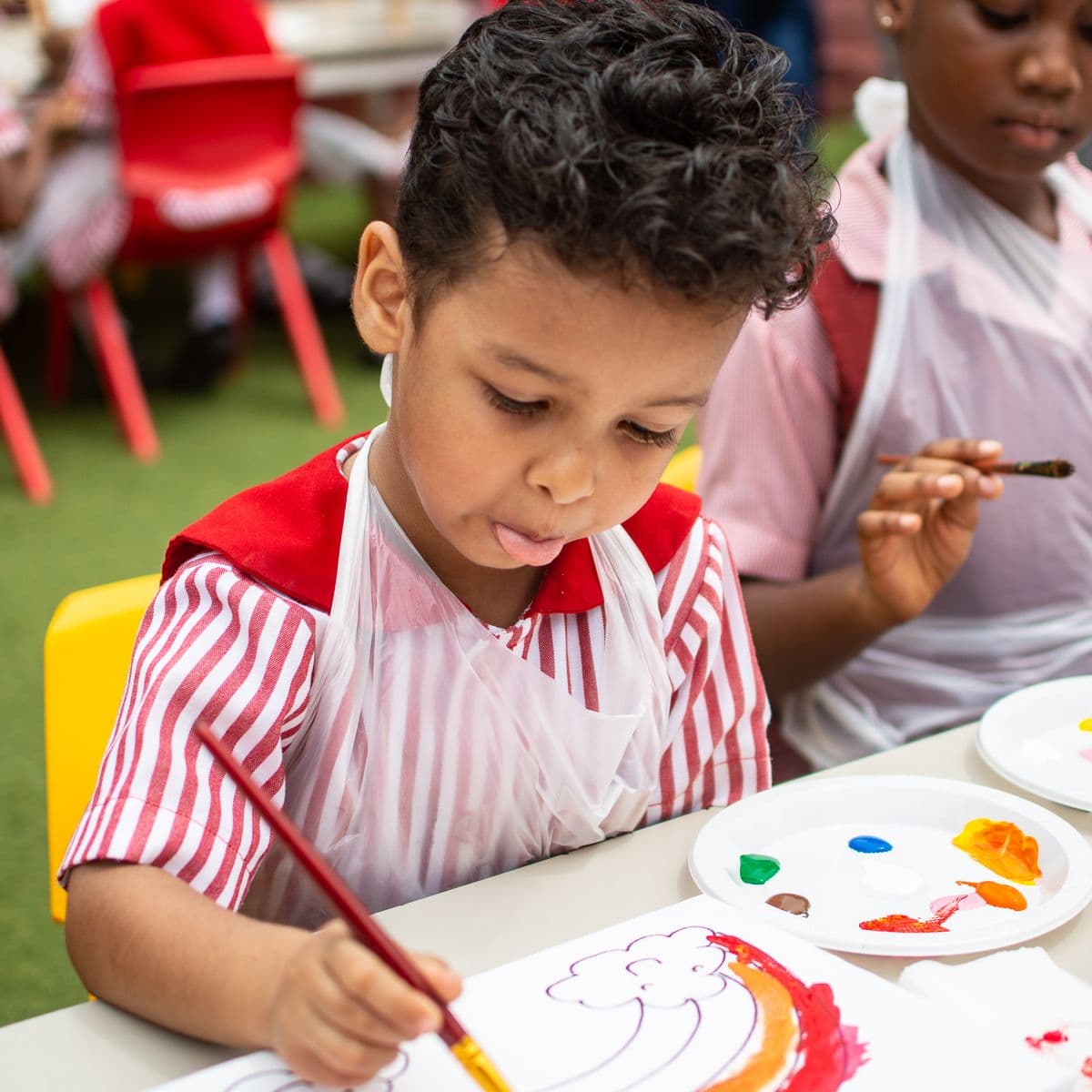 A pupil in a painting apron working on a picture at a table