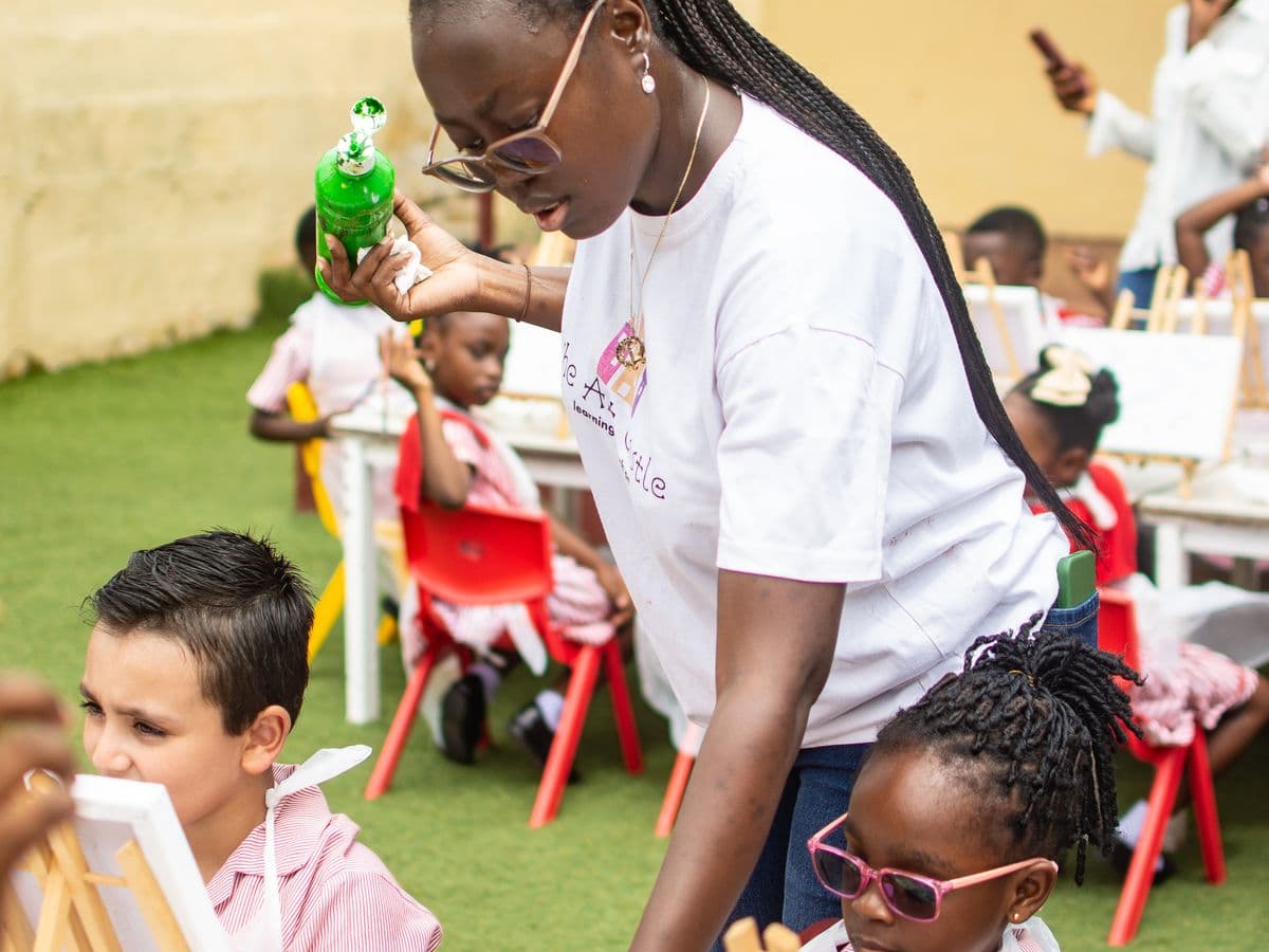 A teacher leaning in to help two young pupils at the painting tables