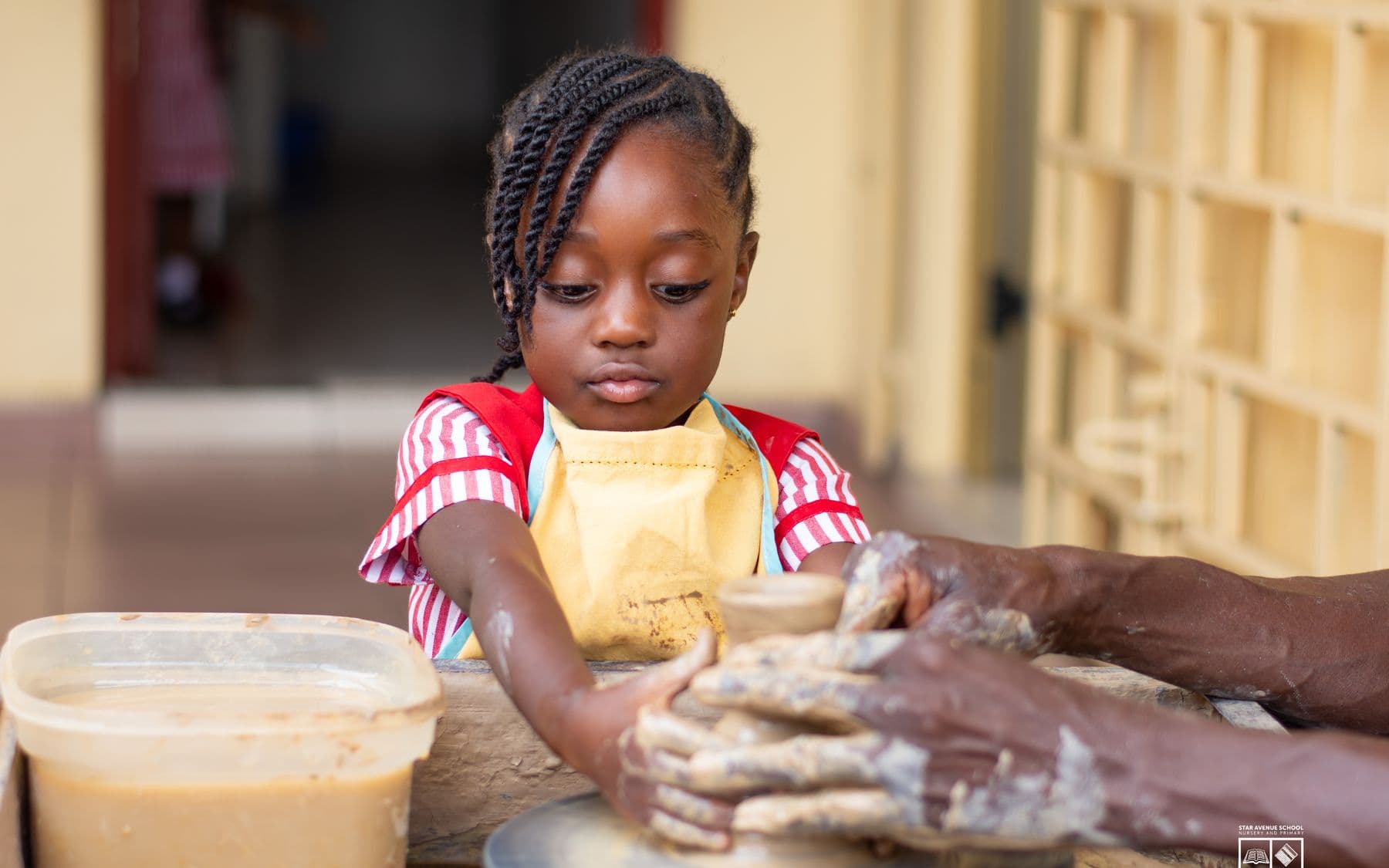 The youngest pupils learning to centre clay on the wheel, guided by a potter