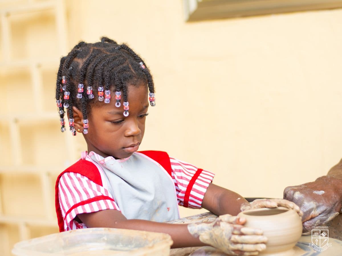 A small child shaping a bowl on a potter's wheel with an adult steadying it