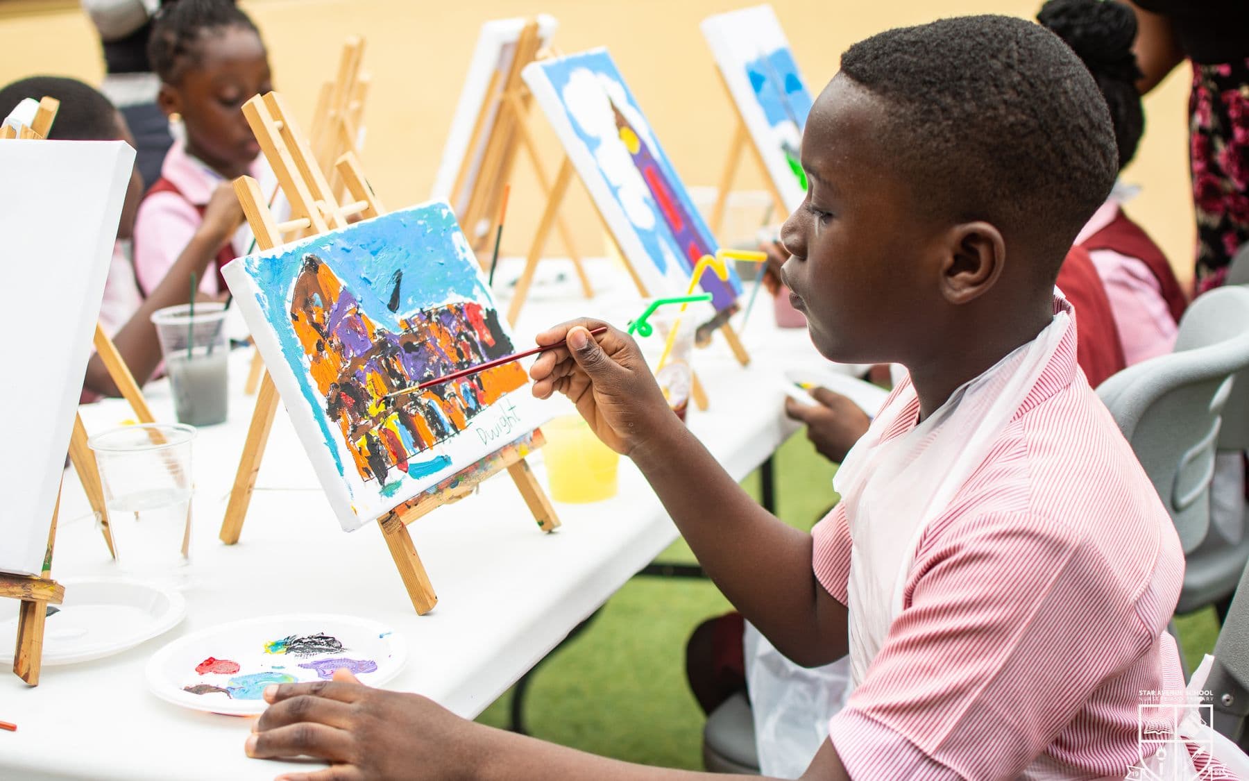 A pupil painting a bright picture at an easel outdoors